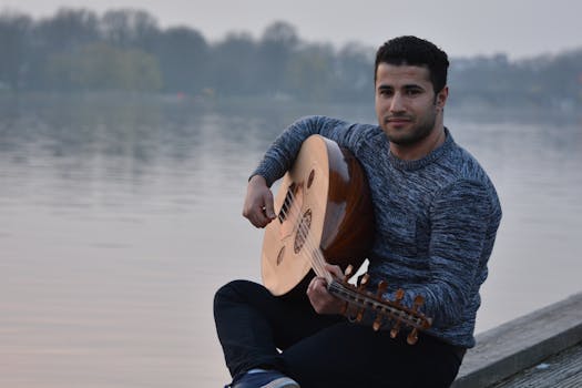Man playing an oud by a tranquil lake, exuding leisure and creativity outdoors.