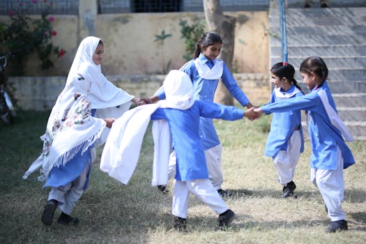 Group of girls in blue uniforms playing joyfully outdoors in a circle.