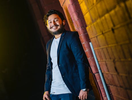A bearded man in a blazer smiles as he leans against a brick wall. Captured in Sri Lanka.
